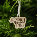 Wooden Christmas ornament with laser engraved cow hanging on a tree