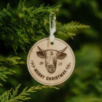 Wooden Christmas ornament with laser engraved cow hanging on a tree