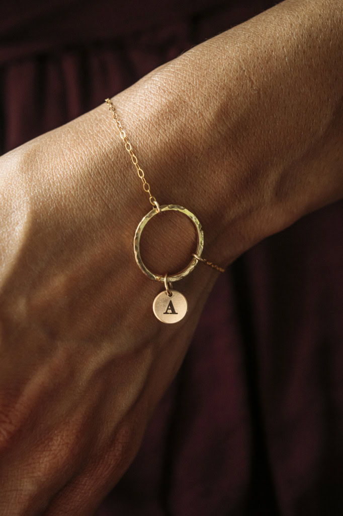 Gold hammered circle necklace with initial charm on wrist.