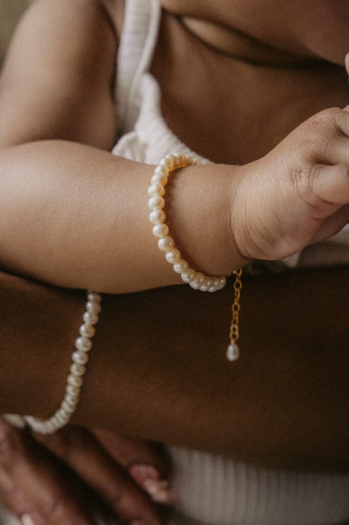 Close-up of a baby's wrist with pearl bracelet and gold chain.
