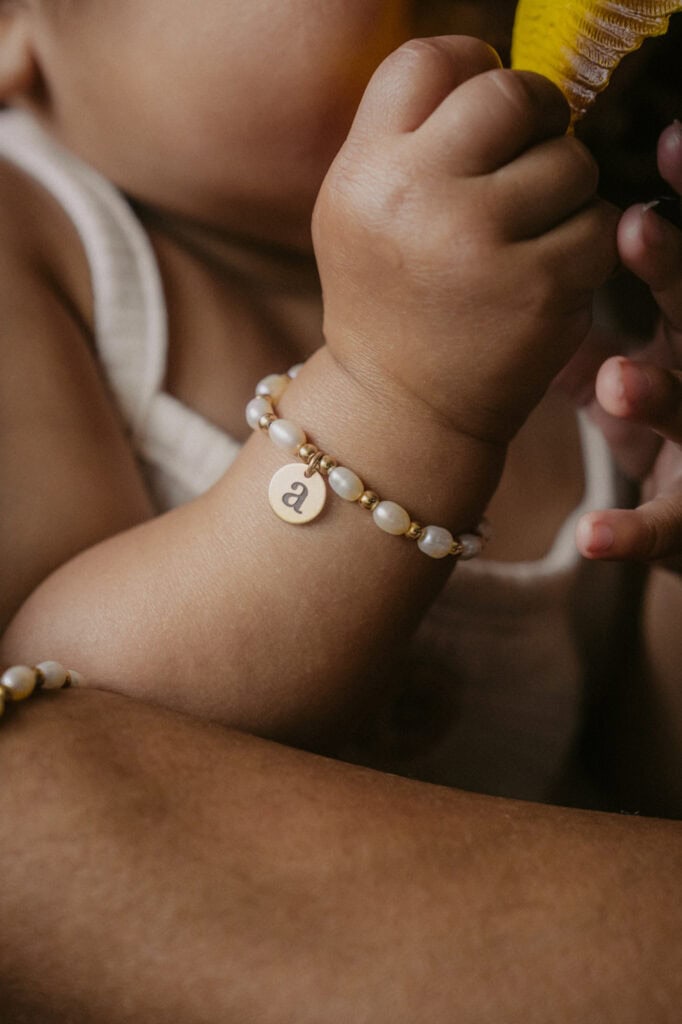 Close-up of child's hand wearing pearl bracelet holding a yellow toy.