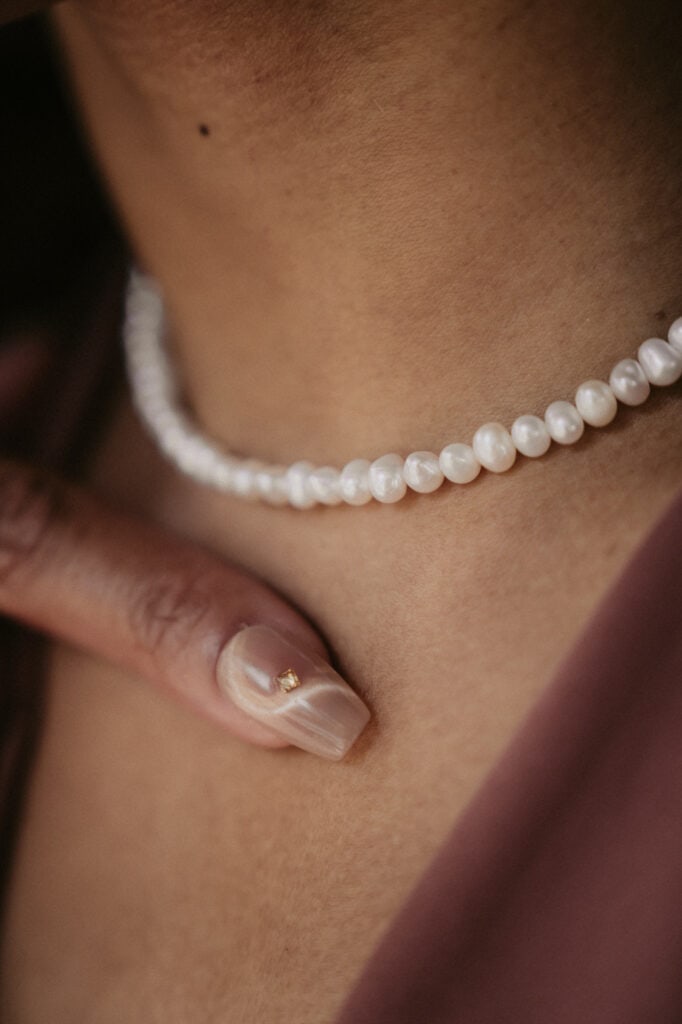Close-up of a pearl necklace and a hand with a ring on the neck.