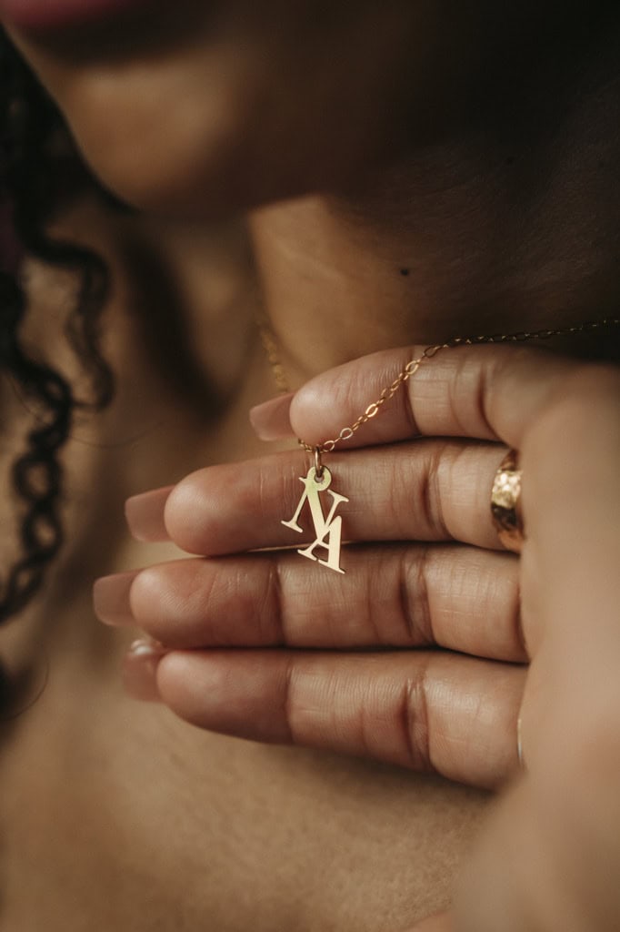 Close-up of a woman's hand holding a gold necklace with NYMAR pendant.